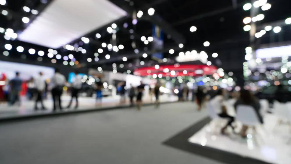 ALT Text: an out of focus image of CES with a crowd of people walking through the convention center  